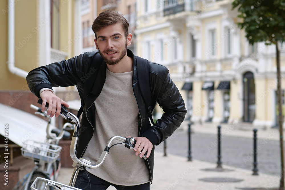 Handsome bike messenger with backpack stands near bicycle and look at camera Handsome bike messenger with backpack stands near bicycle and look at camera