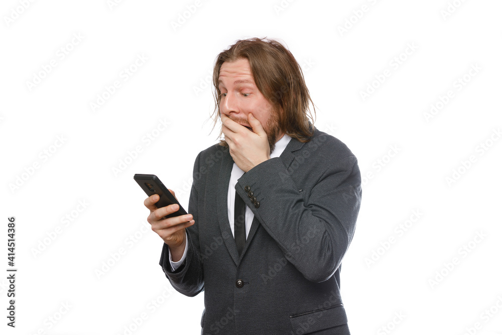 Portrait of surprised businessman with a beard and long hair in formal suit looks at mobile phone isolated on white background. Portrait of surprised businessman with a beard and long hair in formal suit looks at mobile phone isolated on white background.