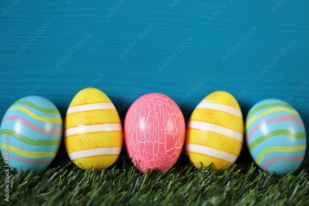 Fototapeta premium Easter holiday.Multicolored striped easter eggs set on green grass on turquoise background..Spring festive easter background. copy space. Easter egg hunt