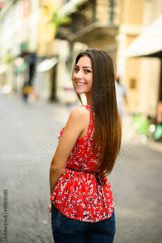 Beautiful charming young lady waking in a cuty street and looking back at the camera