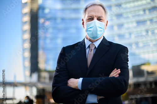 Senior manager with folded arms wearing a protective mask outdoor against Covid 19