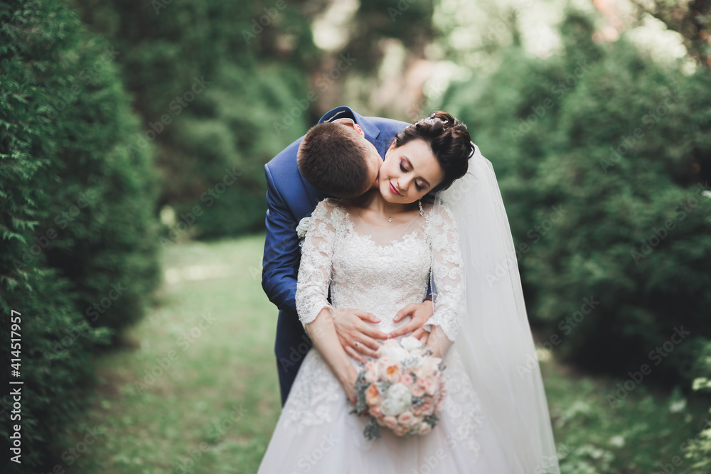 Stylish couple of happy newlyweds walking in the park on their wedding day with bouquet Stylish couple of happy newlyweds walking in the park on their wedding day with bouquet