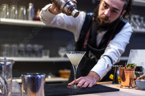 Bartender pouring fresh alcoholic drink into the glasses with ice cubes on the bar counter