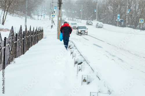 a man with difficulty walks through deep snow, snowdrifts on the sidewalk after a heavy snowfall. poor operation of public utilities in winter