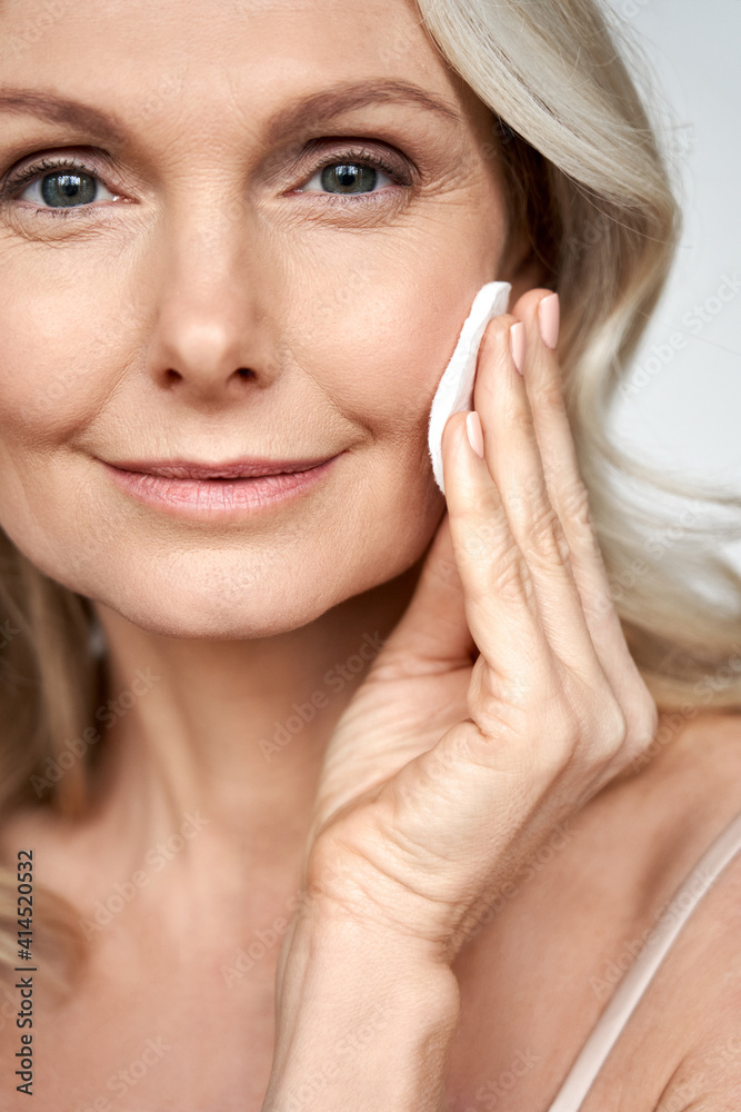 Pretty 50s middle aged old woman holding cotton pad sponge cleansing face skin purifying with cleanser, happy mature lady removing makeup enjoy healthy clean anti age dry skincare lifting routine. Pretty 50s middle aged old woman holding cotton pad sponge cleansing face skin purifying with cleanser, happy mature lady removing makeup enjoy healthy clean anti age dry skincare lifting routine.