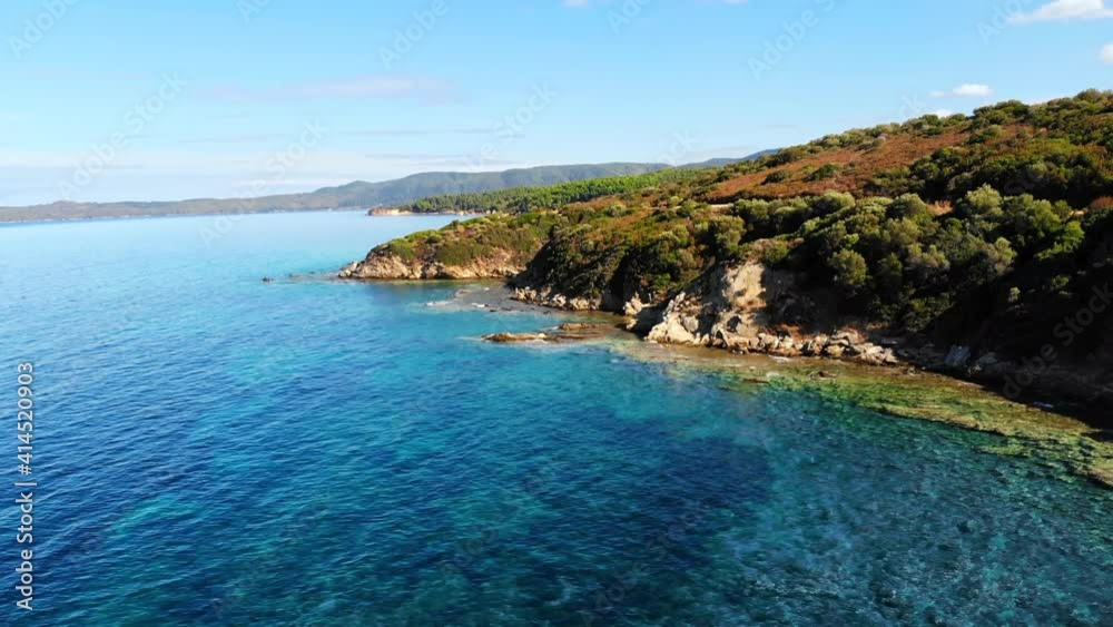 Aerial drone view of the Aegean sea rocky coast with greenery along the shore and hills in the distance, blue water in Greece Aerial drone view of the Aegean sea rocky coast with greenery along the shore and hills in the distance, blue water in Greece