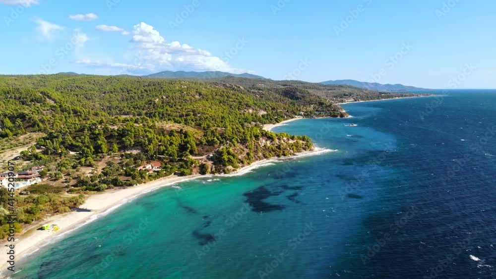 Aerial drone view of the Aegean sea rocky coast with greenery, town and road along the shore, waves of the sea in Greece
