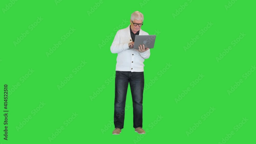Old man standing and using a laptop computer on a Green Screen, Chroma Key. Old man standing and using a laptop computer on a Green Screen, Chroma Key.