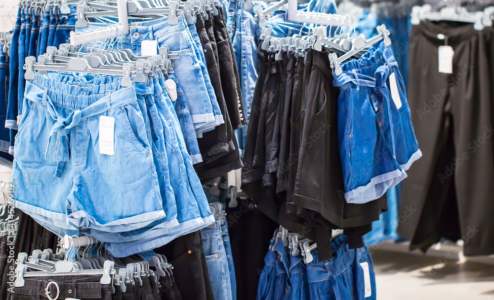 Women's jeans wear on hangers and shelves in a clothing store. Set denim casual wear for ladies. Fashionable and style. Boutique in the mall. Blurred background with copy space. Discounts and sale.