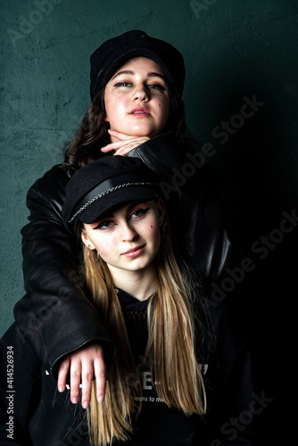 Two charming teenage girls with bright makeup, dressed in a grunge style, against a dark wall. © FO_DE