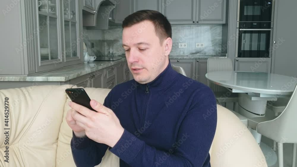 young adult man relaxing on comfortable couch, using mobile application in living room. Happy guy scrolling in social network or web surfing internet young adult man relaxing on comfortable couch, using mobile application in living room. Happy guy scrolling in social network or web surfing internet