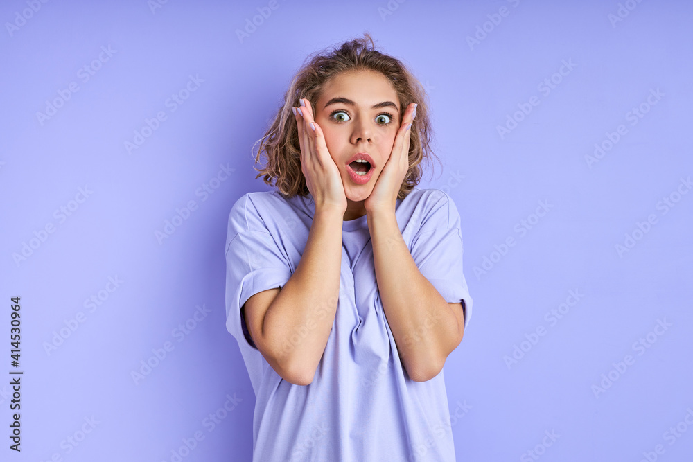 woman starring touching cheeks isolated on pastel purple color background, she is surprised by something, stand with wide opened mouth and eyes woman starring touching cheeks isolated on pastel purple color background, she is surprised by something, stand with wide opened mouth and eyes