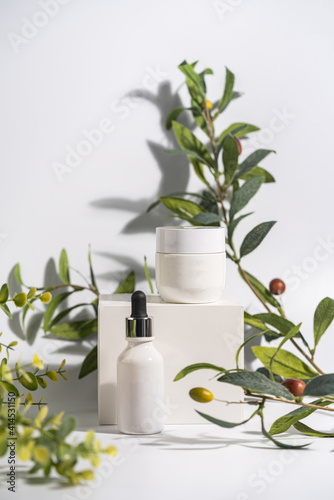 Cosmetic cream and serum or essential oil bottle on white background with olive brenches. Bright shadows. Beauty product concept.