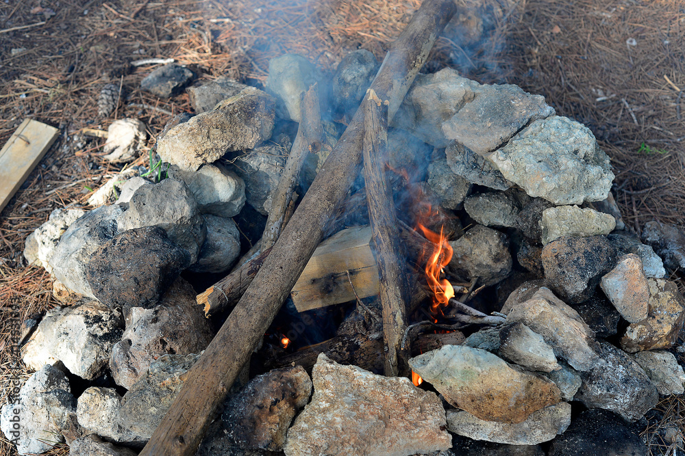 Fireplace in the forest. Smoking campfire on the nature. Camping place with wooden benches in summer forest. Campsite with campfire. Grey and brown big stones and wood for a bonfire in a fireplace Fireplace in the forest. Smoking campfire on the nature. Camping place with wooden benches in summer forest. Campsite with campfire. Grey and brown big stones and wood for a bonfire in a fireplace
