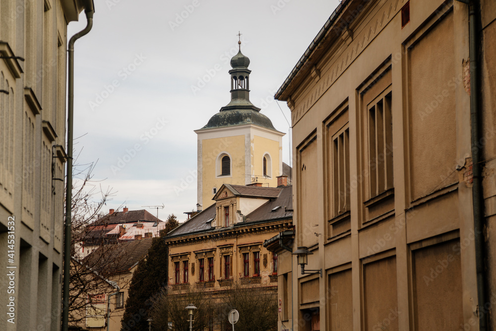 Narrow medieval picturesque street with baroque and renaissance historical buildings in winter day, bell tower of church of St. Nicholas, Bohemian Paradise, Turnov, Czech Republic
