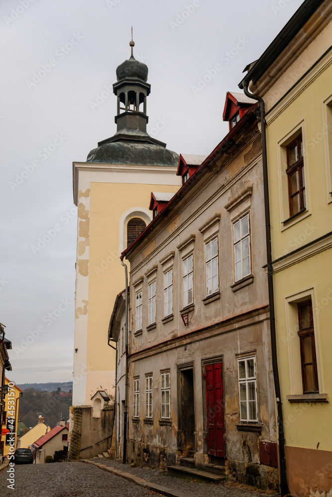 Narrow medieval picturesque street with baroque and renaissance historical buildings in winter day, bell tower of church of St. Nicholas, Bohemian Paradise, Turnov, Czech Republic