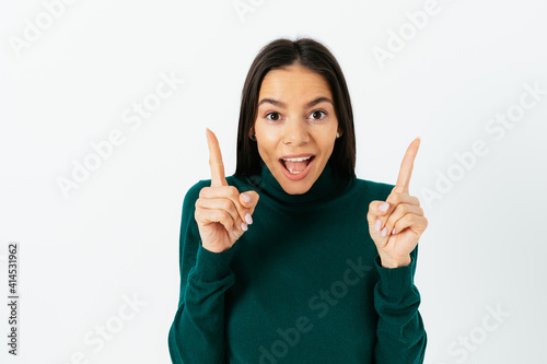Brunette woman pointing with two hands up and looking at camera