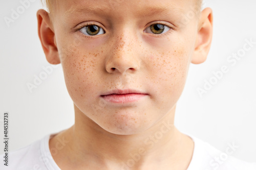 confident child with freckles and big green eyes looking in camera with serious expression, caucasian kid boy isolated over white studio background