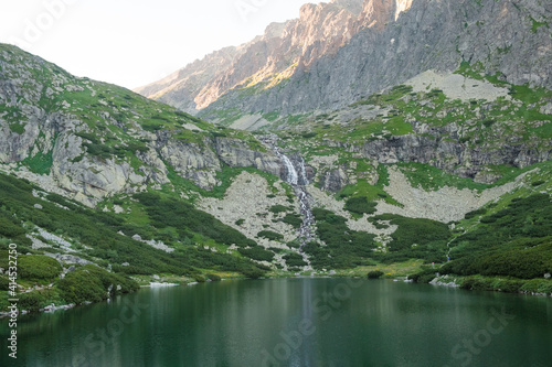 Reflections in the calm lake water, waterfall and mountains at sunset.