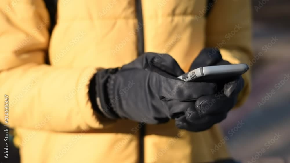 Food delivery man on a scooter in a park using his smartphone. Yellow jacket and black gloves. Winter Food delivery man on a scooter in a park using his smartphone. Yellow jacket and black gloves. Winter