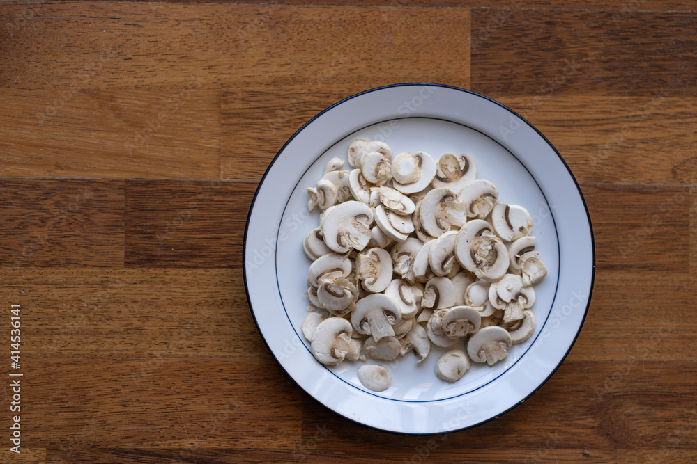 Fototapeta premium sliced ​​mushrooms on white plate and wooden background