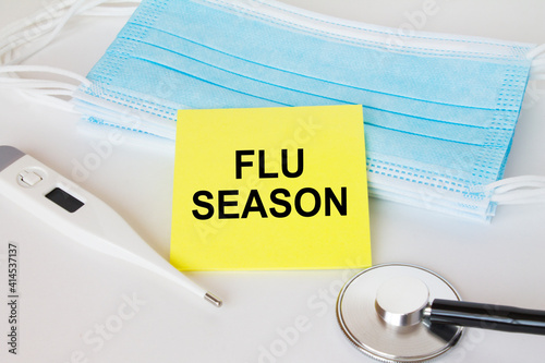 Yellow sticker with text Flu Season lying with the mask, stethoscope and thermometer