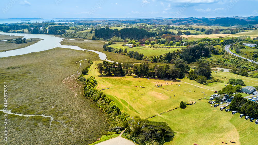 Fototapeta premium Aerial view of a small river running to the sea through green countryside spotted with little farms. Auckland, New Zealand.