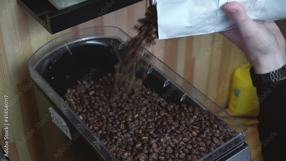 male barista pouring coffee beans into the grinder male barista pouring coffee beans into the grinder