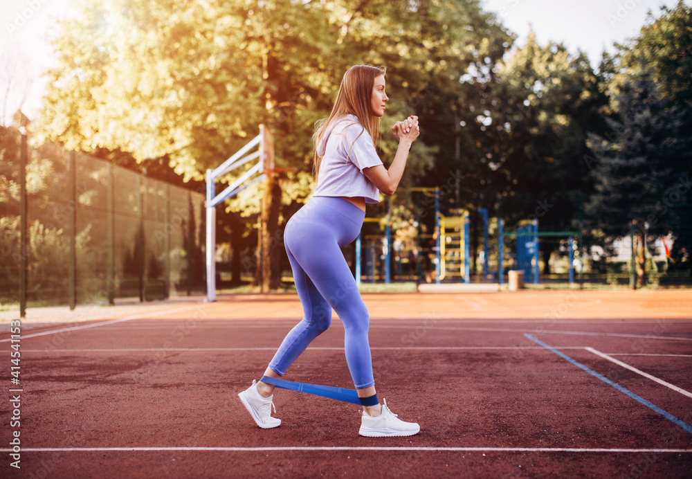 Athletic pregnant woman doing an exercise with a gym elastic band in a park on a summer day .Concept of healthy lifestyle