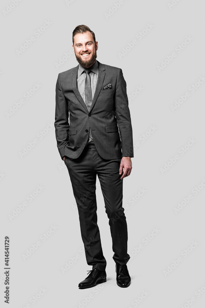 Attractive caucasian businessman with a beard and a friendly smile wearing a grey suit and tie, standing casually with one hand in his pocket. Attractive caucasian businessman with a beard and a friendly smile wearing a grey suit and tie, standing casually with one hand in his pocket.