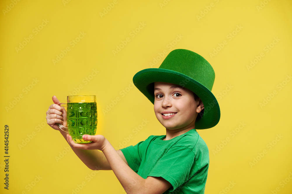 Smiling happy caucasian boy in Irish green hat holds a glass with green drink poses on camera. Saint Patrick's Day Smiling happy caucasian boy in Irish green hat holds a glass with green drink poses on camera. Saint Patrick's Day