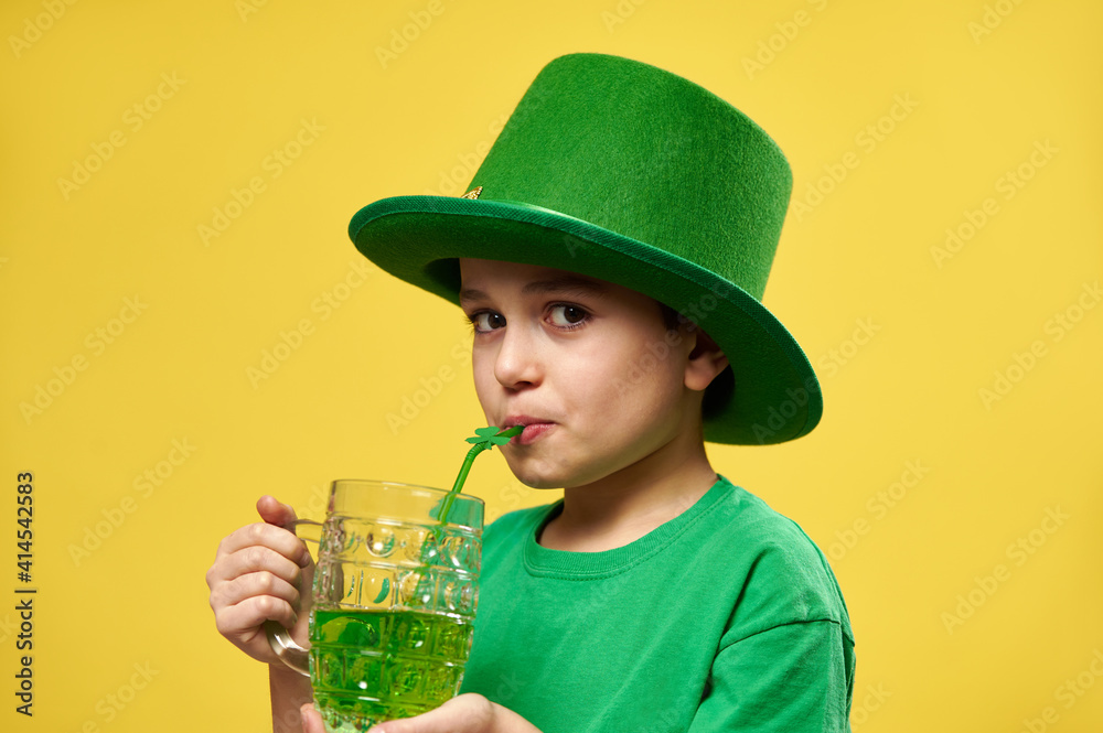 Little boy looks at the camera while drinking green drink from a straw with clover leaf ornament celebrating a Saint Patrick's Day. Copy space Little boy looks at the camera while drinking green drink from a straw with clover leaf ornament celebrating a Saint Patrick's Day. Copy space