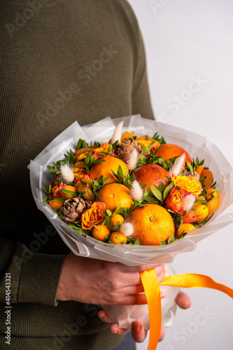 Fototapeta Naklejka Na Ścianę i Meble -  Bouquet of fruits and flowers in men's hands on a white background. Copy space for a text.