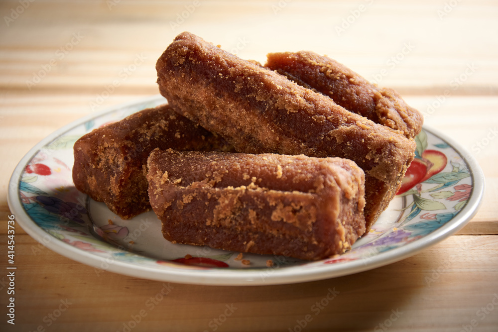 View of panela slices in a small plate on wooden table. Also known as rapadura, it is unrefined whole cane sugar typical of Central and Latin America. View of panela slices in a small plate on wooden table. Also known as rapadura, it is unrefined whole cane sugar typical of Central and Latin America.