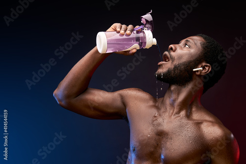 sportsman pours water on himself after training, african male holding water bottle in hands, take a break after workout photo