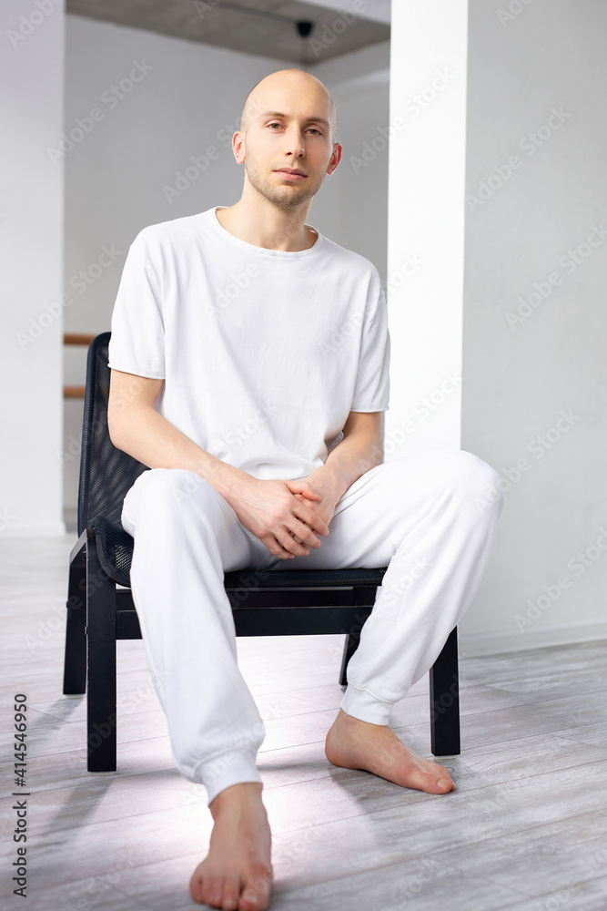 Fototapeta premium calm male sitting in chair in studio and looking at camera, after yoga class, in white clothing. sport, yoga, healthy lifestyle concept. portrait