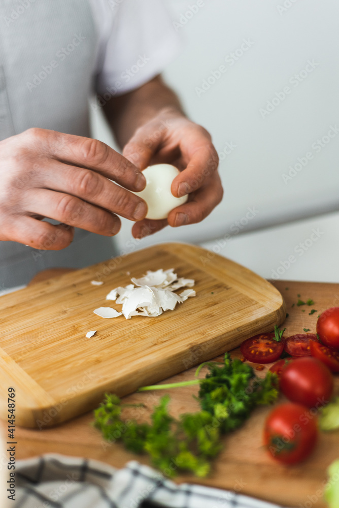 A man peels a boiled egg on a cutting board. Cooking Caesar salad. Cooking in the kitchen