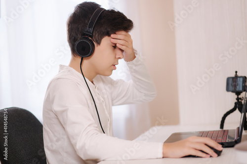 Face palm of teenage steammer during the game. Boy in headphones play on laptop at home photo