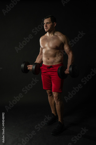 Fitness man presses dumbbells in red panties business caucasian smart, torso studio boy, success lonely background black bodybuilder