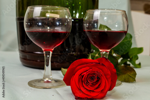 two glasses and a large bottle of wine and a rose