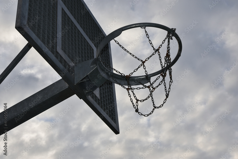 Street basketball hoop with metal chains, close up, cloudy sky in background Street basketball hoop with metal chains, close up, cloudy sky in background