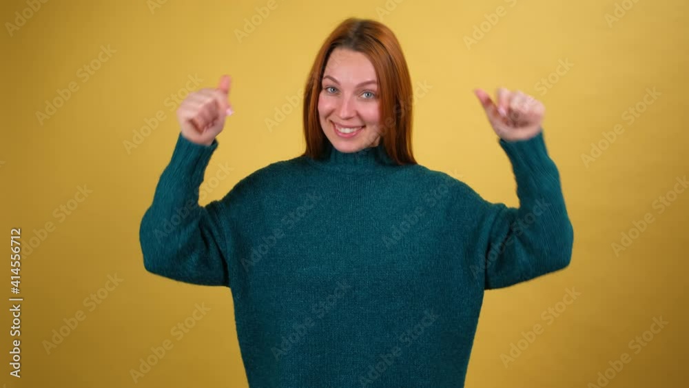 Excited positive woman pointing fingers down asking to subscribe on his blog and rate posts. Indoor studio shot isolated on yellow background