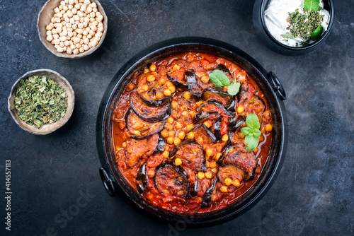 Modern style slow cooked Lebanese vegetarian eggplant stew maghmour served with chickpeas and yoghurt as top view in a design pot with copy space