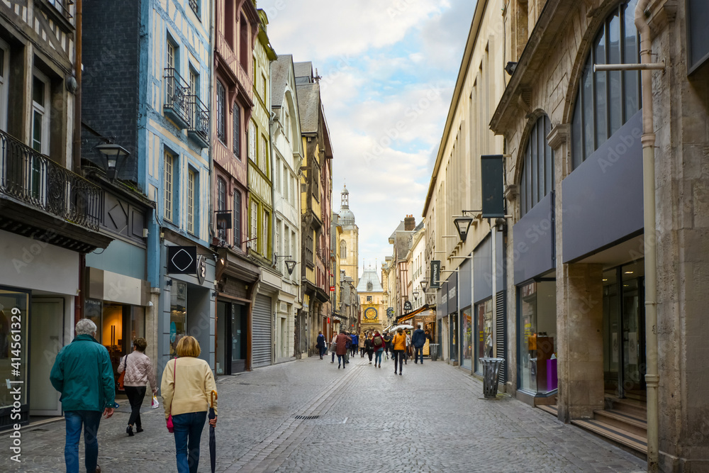 Tourists enjoy a stroll along the shops on the Rue du Gros Orloge in Rouen France with the astronomical clock in the background.