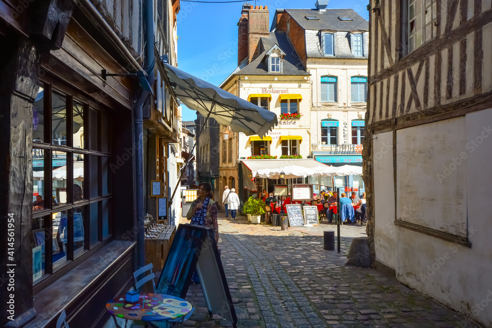 A woman window shops on a sunny day in the Normandy town of Honfleur France with an outdoor sidewalk cafe behind her