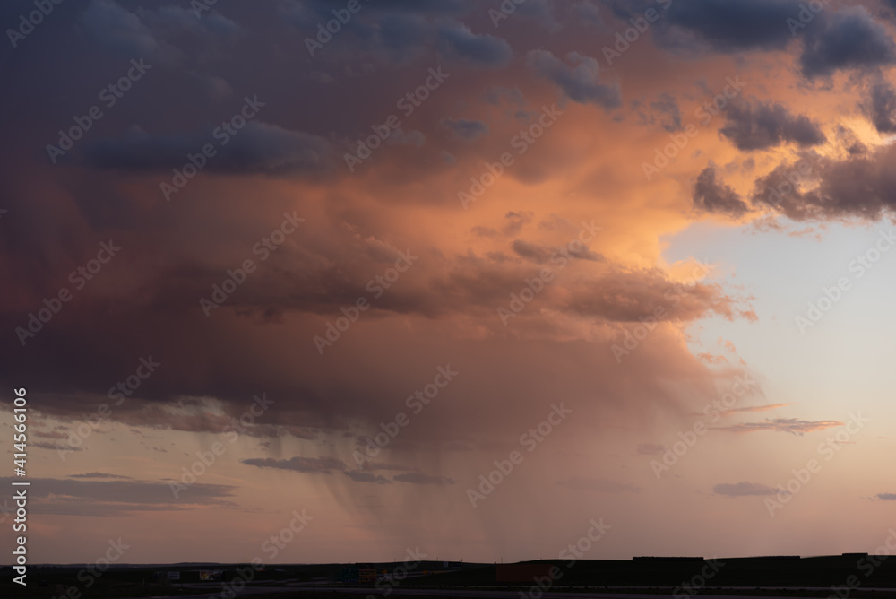 A flat landscape seen before a cloudy storm approaching with pink, orange dark clouds, shining sun and dark country, rural land below. Great for sky replacement for editing photos or drawing. 