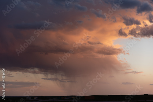 A flat landscape seen before a cloudy storm approaching with pink  orange dark clouds  shining sun and dark country  rural land below. Great for sky replacement for editing photos or drawing. 