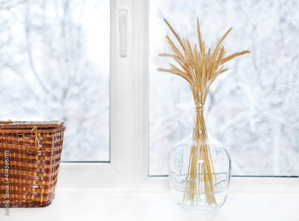 Wheat ears in a glass vase with wicker box on a winter windowsill. Eco interior concept. Wheat ears in a glass vase with wicker box on a winter windowsill. Eco interior concept.