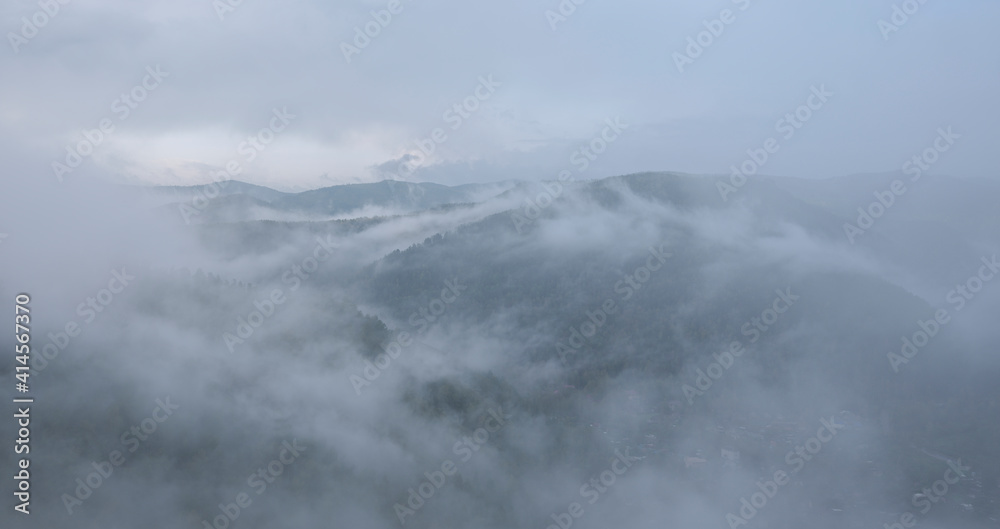 Fog in the mountains. Green forest in the highlands, residential buildings in the valley.