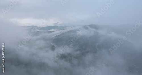 Fog in the mountains. Green forest in the highlands, residential buildings in the valley.